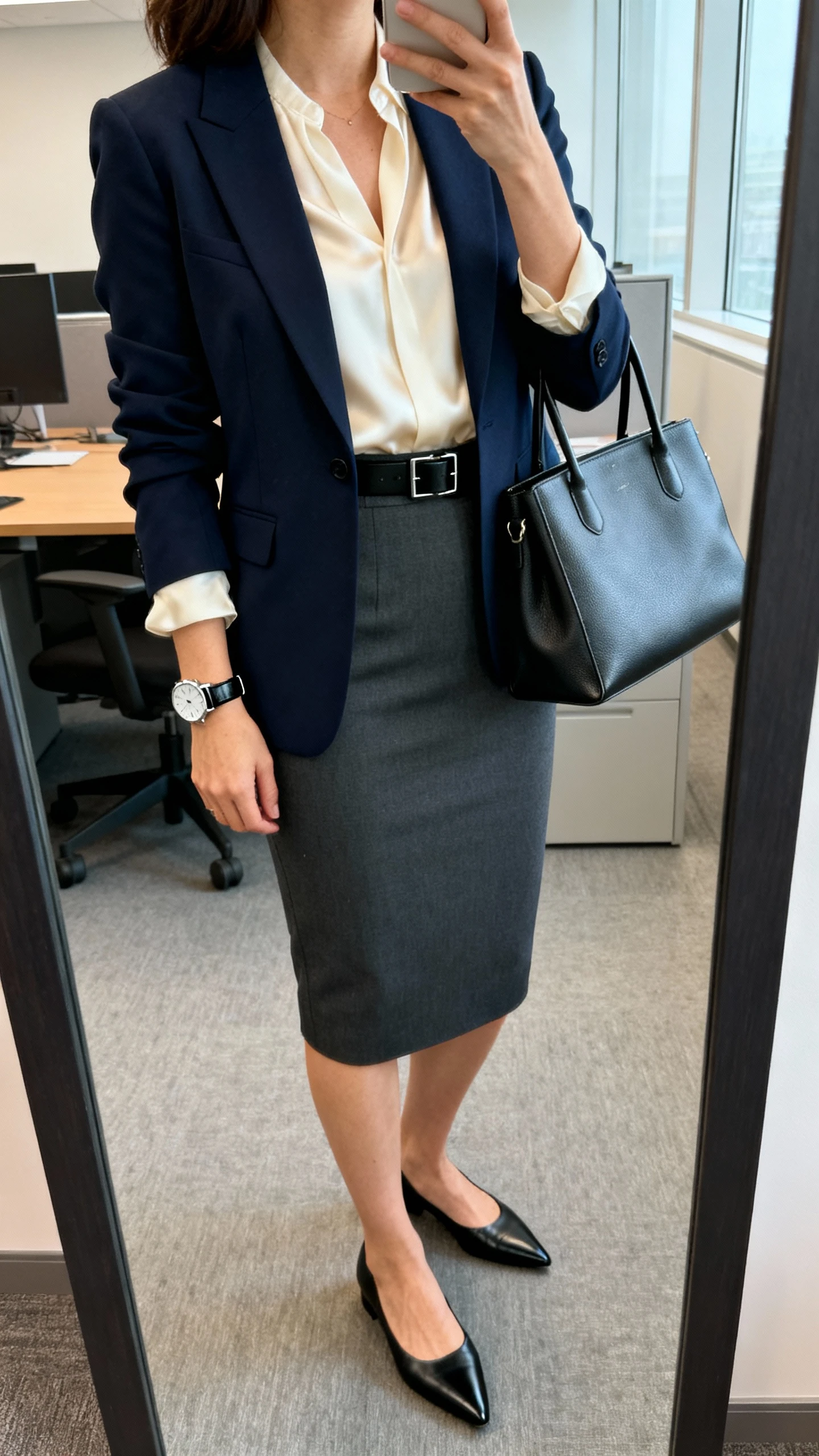 iPhone back-view mirror selfie of a woman in an elevated workday capsule: navy tailored blazer, silk cream blouse, charcoal pencil skirt, black pointed-toe flats, minimalist steel watch with black leather strap, slim black belt, structured tote, face not visible, full-length mirror, indoor office-like lighting, iPhone photo quality.