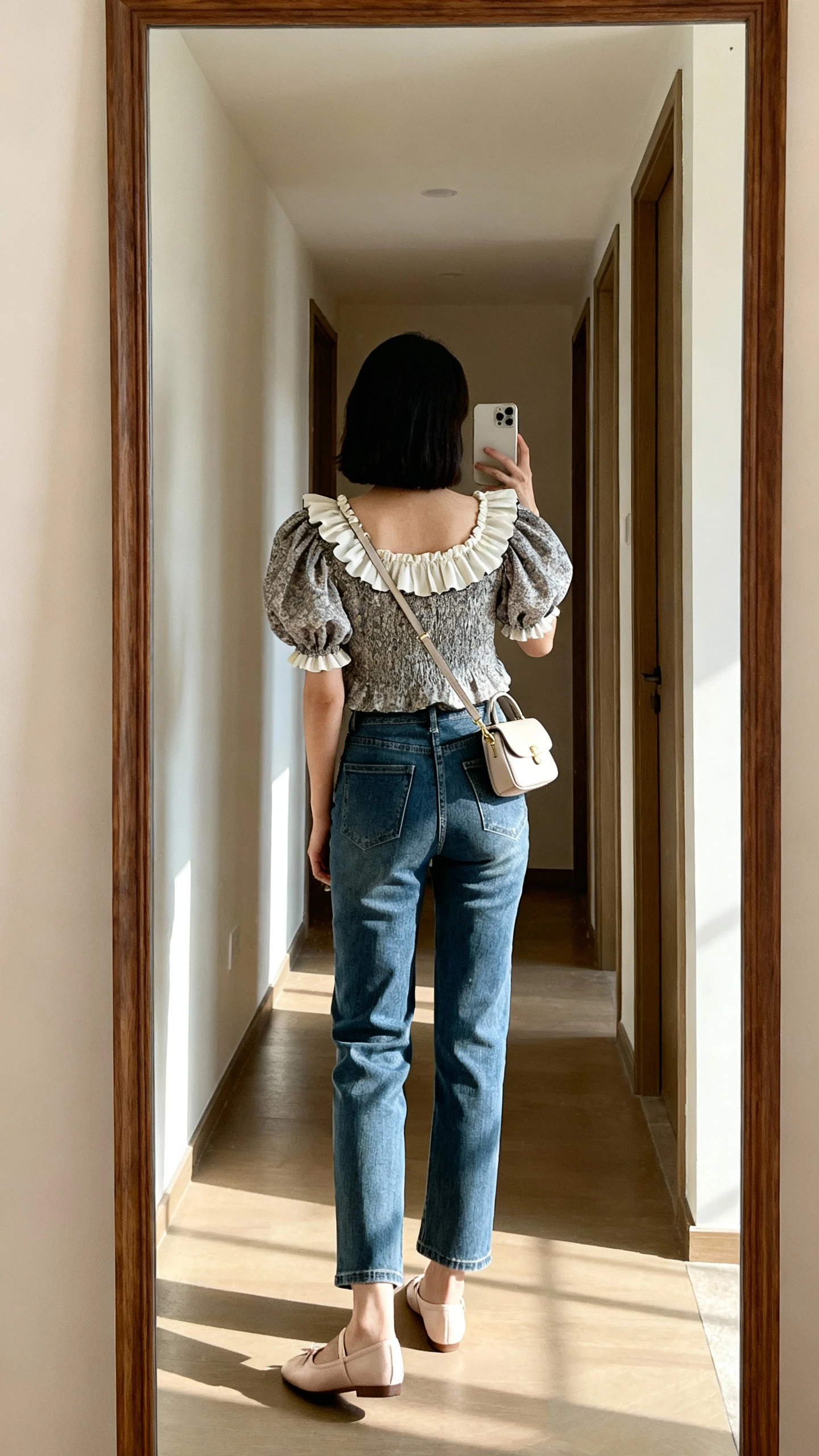 iPhone back-view mirror selfie of a woman wearing straight-leg jeans with a statement top (ruffled neckline and puff sleeves), ballet flats and a petite shoulder bag, face not visible, hallway full-length mirror, soft afternoon daylight, iPhone photo quality