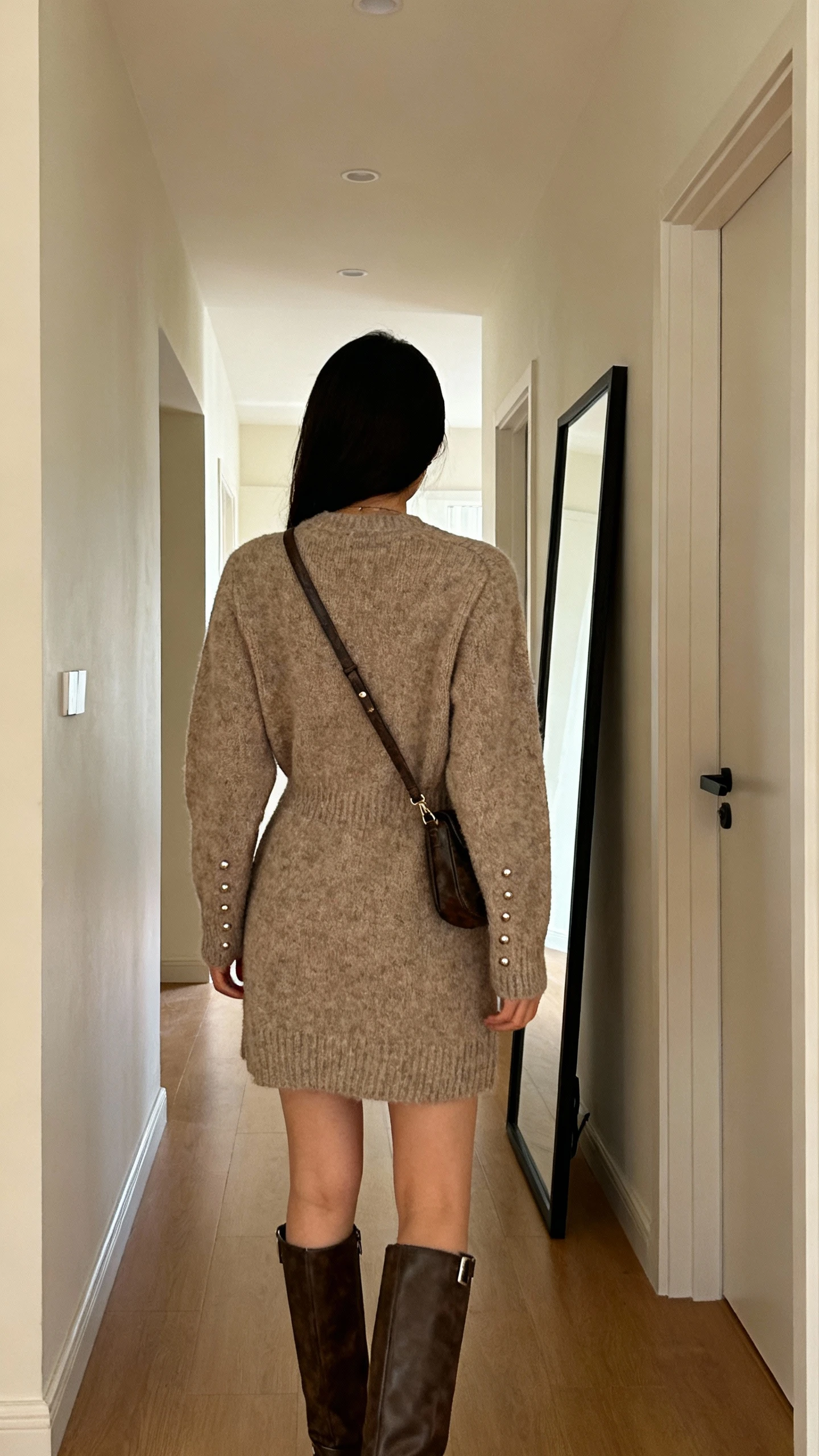 iPhone back view of a woman in a cozy knit dress paired with knee-high boots, simple studs, and a crossbody bag; face not visible, hallway full-length mirror, warm indoor lighting, casual iPhone photo.