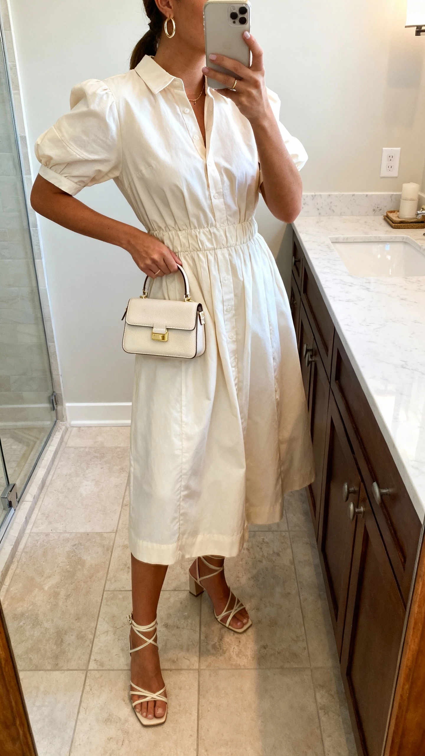 iPhone bathroom mirror selfie of a woman wearing a crisp poplin midi dress with a mini top-handle bag, delicate hoop earrings, and strappy heels, face not visible, side angle, morning indoor light, iPhone photo quality.