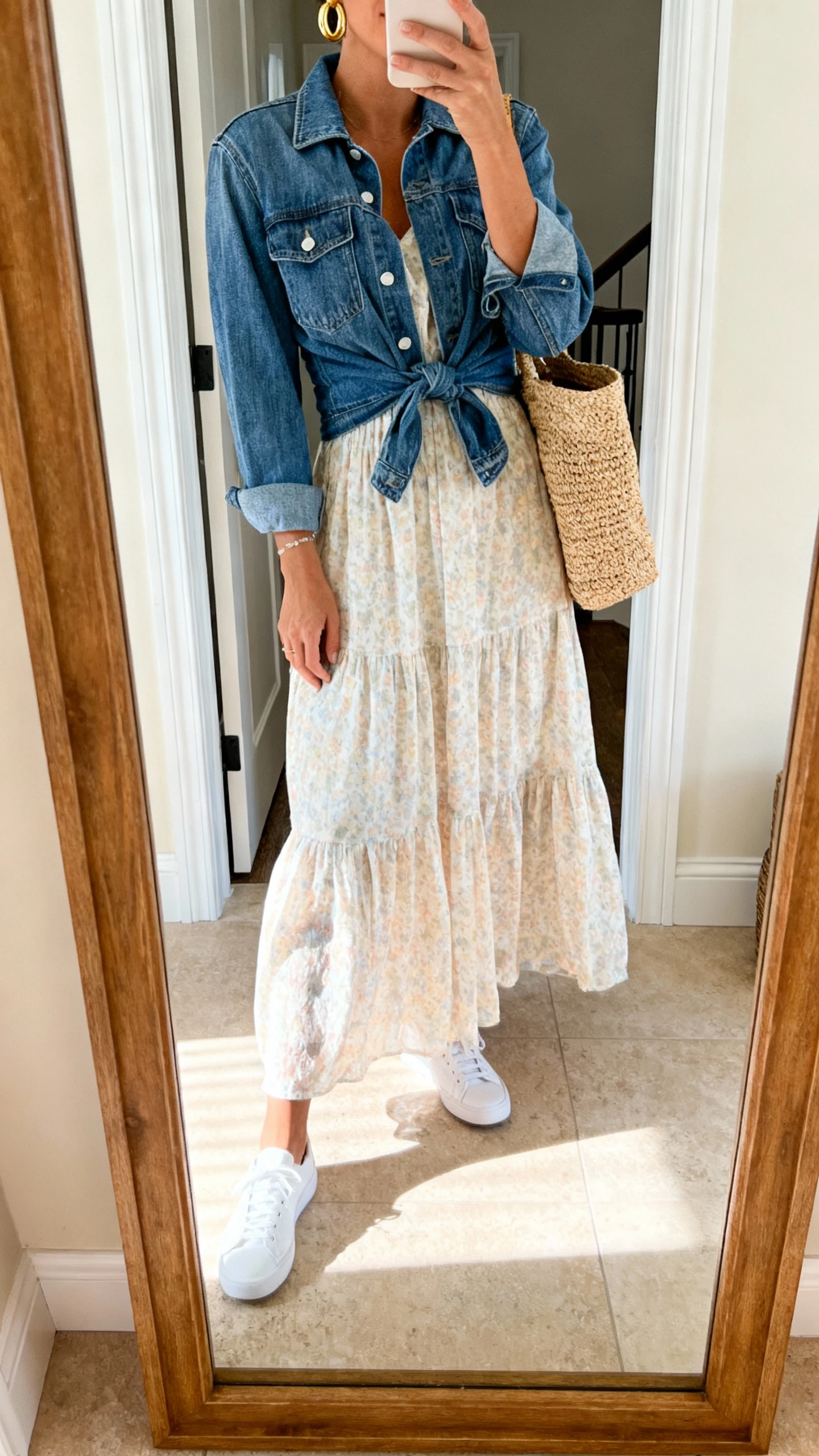 iPhone mirror selfie of a woman wearing a flowy sundress with white sneakers, denim jacket tied at waist, straw tote, gold hoop earrings, face not visible, cropped at neck, entryway full-length mirror, bright morning light, iPhone photo quality