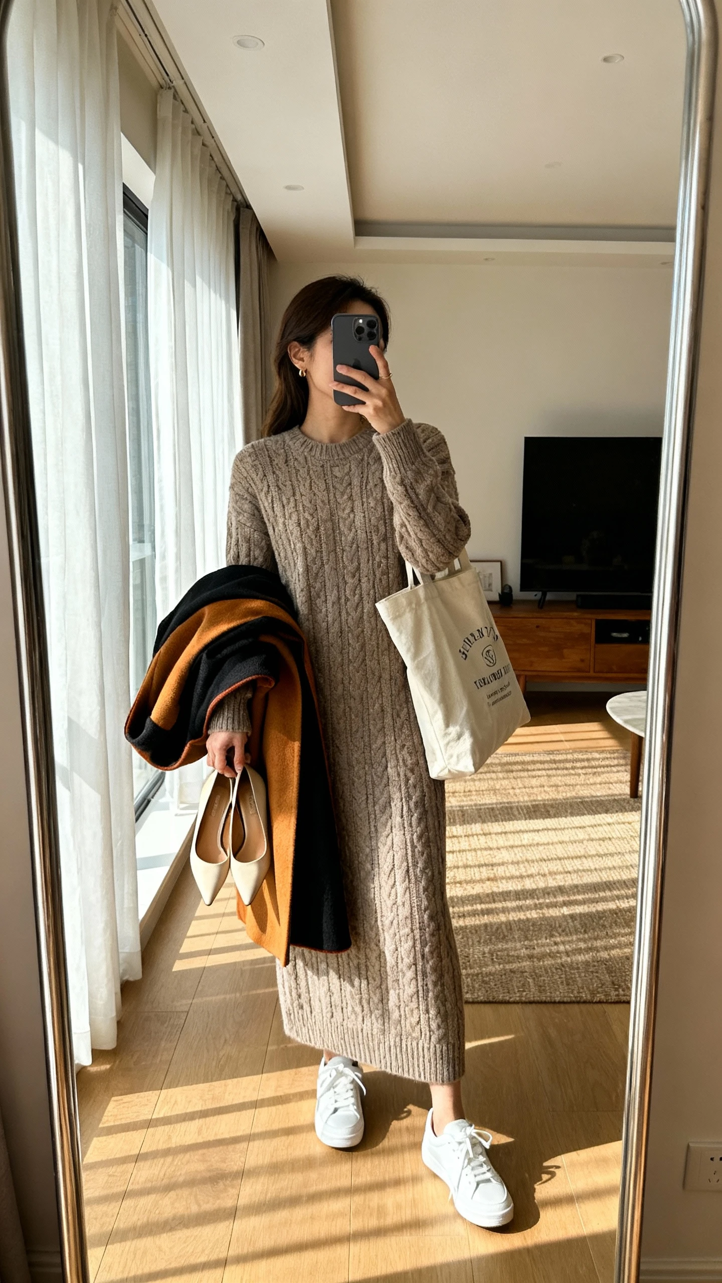iPhone mirror selfie of a woman wearing a knit maxi dress with white sneakers and tote bag for day; draped over arm a statement coat and heels for night, face not visible, side angle, living room mirror, afternoon window light, iPhone photo quality.