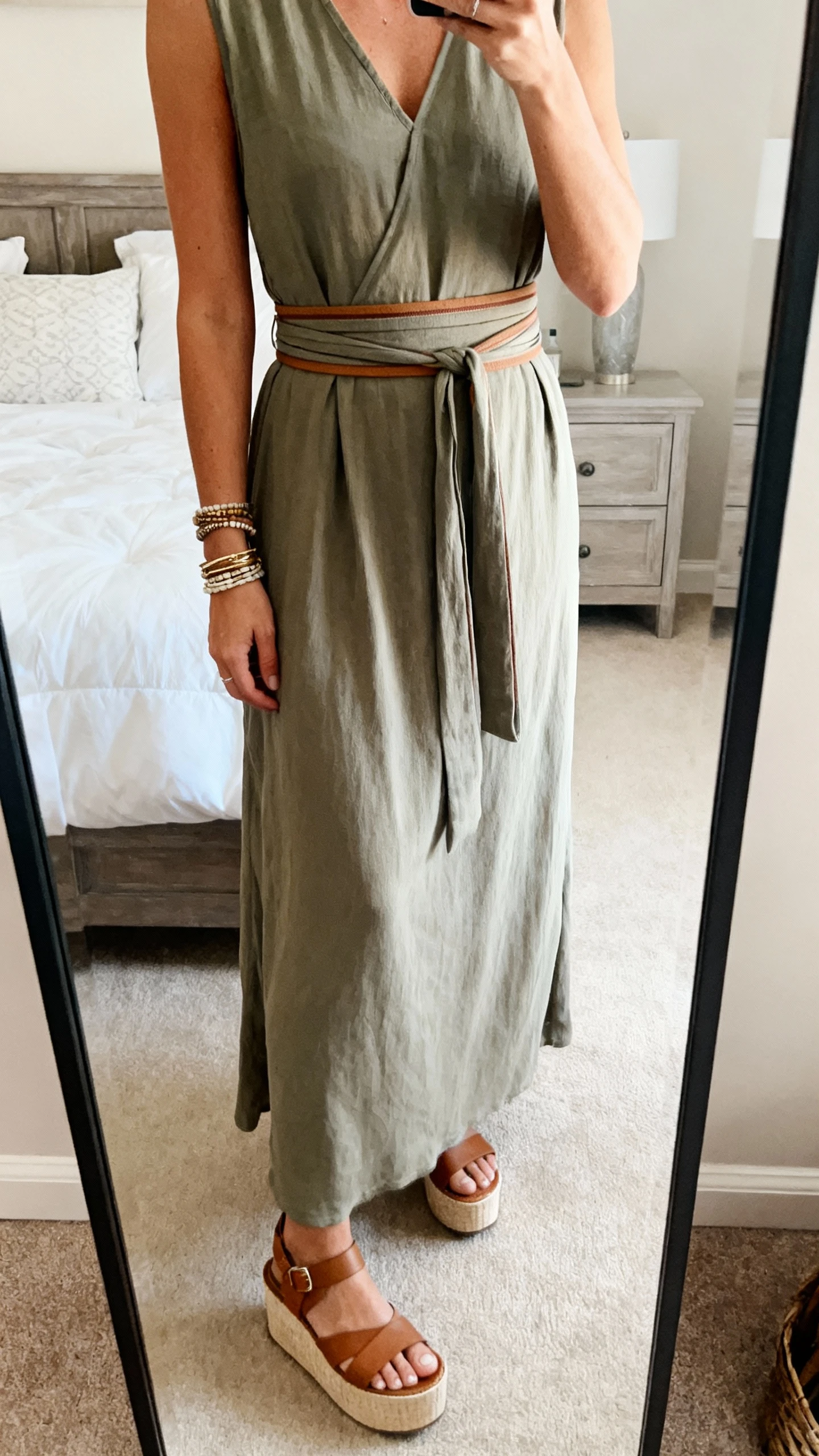 iPhone mirror selfie of a woman wearing a maxi dress with a double-wrap skinny belt defining the waist, platform sandals, layered bracelets, face not visible, cropped at shoulders, bedroom mirror, soft natural light, iPhone photo quality.