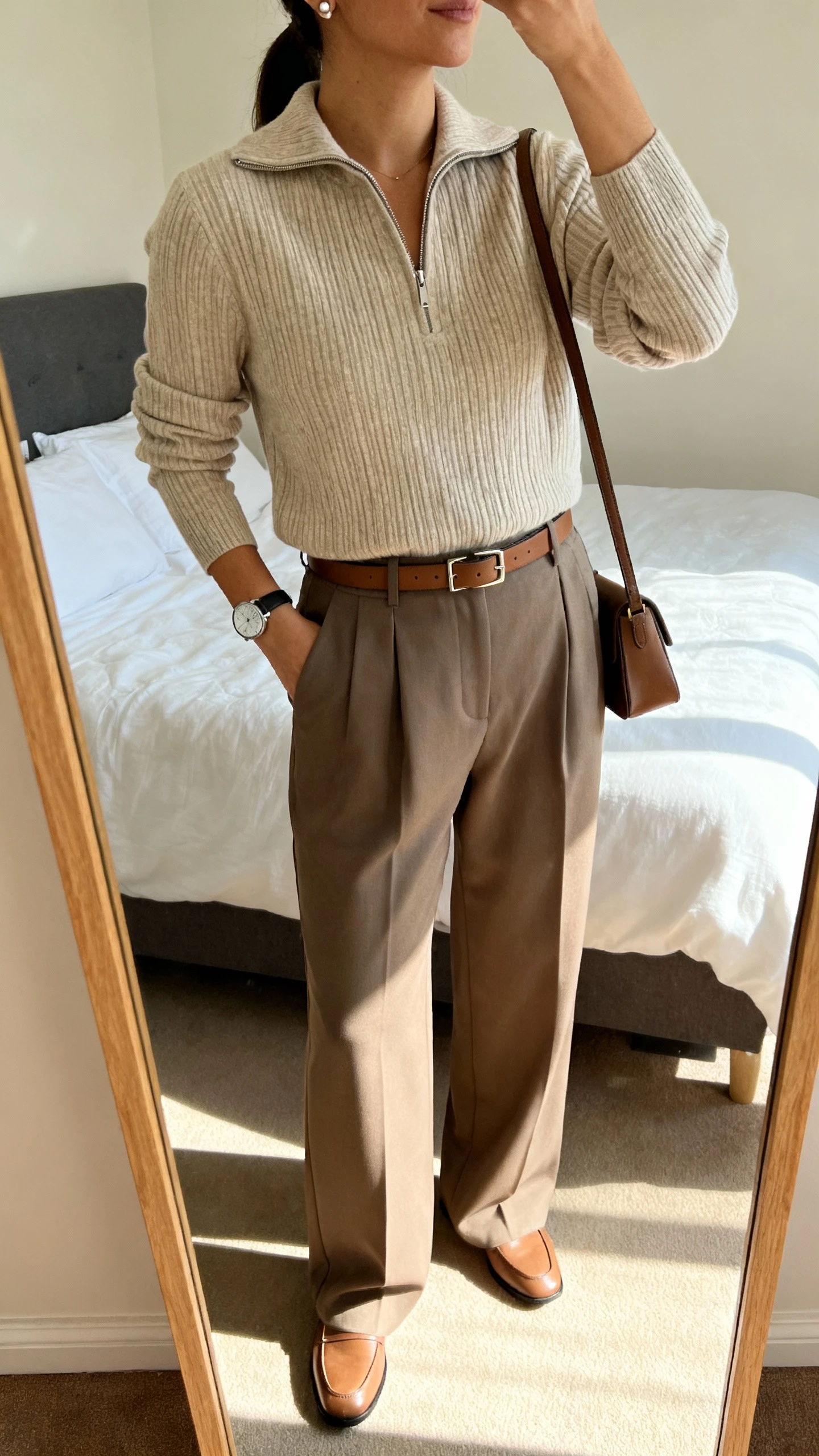 iPhone mirror selfie of a woman wearing a ribbed half-zip pullover tucked into tailored wide-leg trousers, minimalist leather belt, loafers, delicate stud earrings, sleek wristwatch, small shoulder bag, face not visible, cropped at shoulders, bedroom mirror with soft afternoon light, iPhone photo quality.