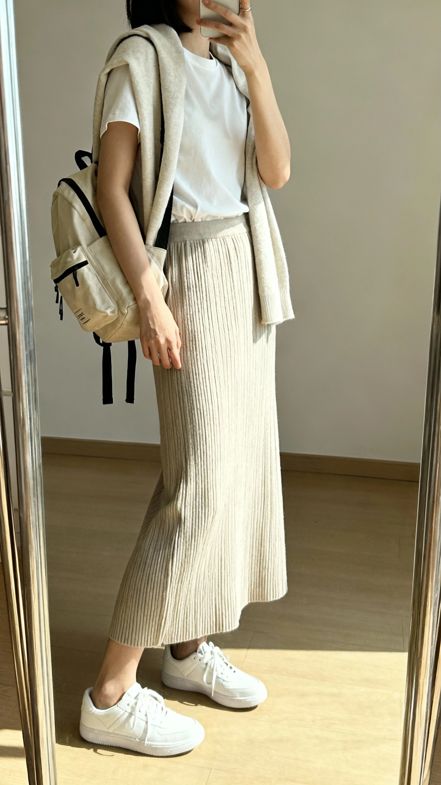 iPhone mirror selfie of a woman wearing a ribbed knit skirt with a tucked-in tee, lightweight cardigan draped over shoulders, casual white sneakers, and a canvas backpack, face not visible, side angle, full-length mirror, bright natural light, iPhone photo quality.