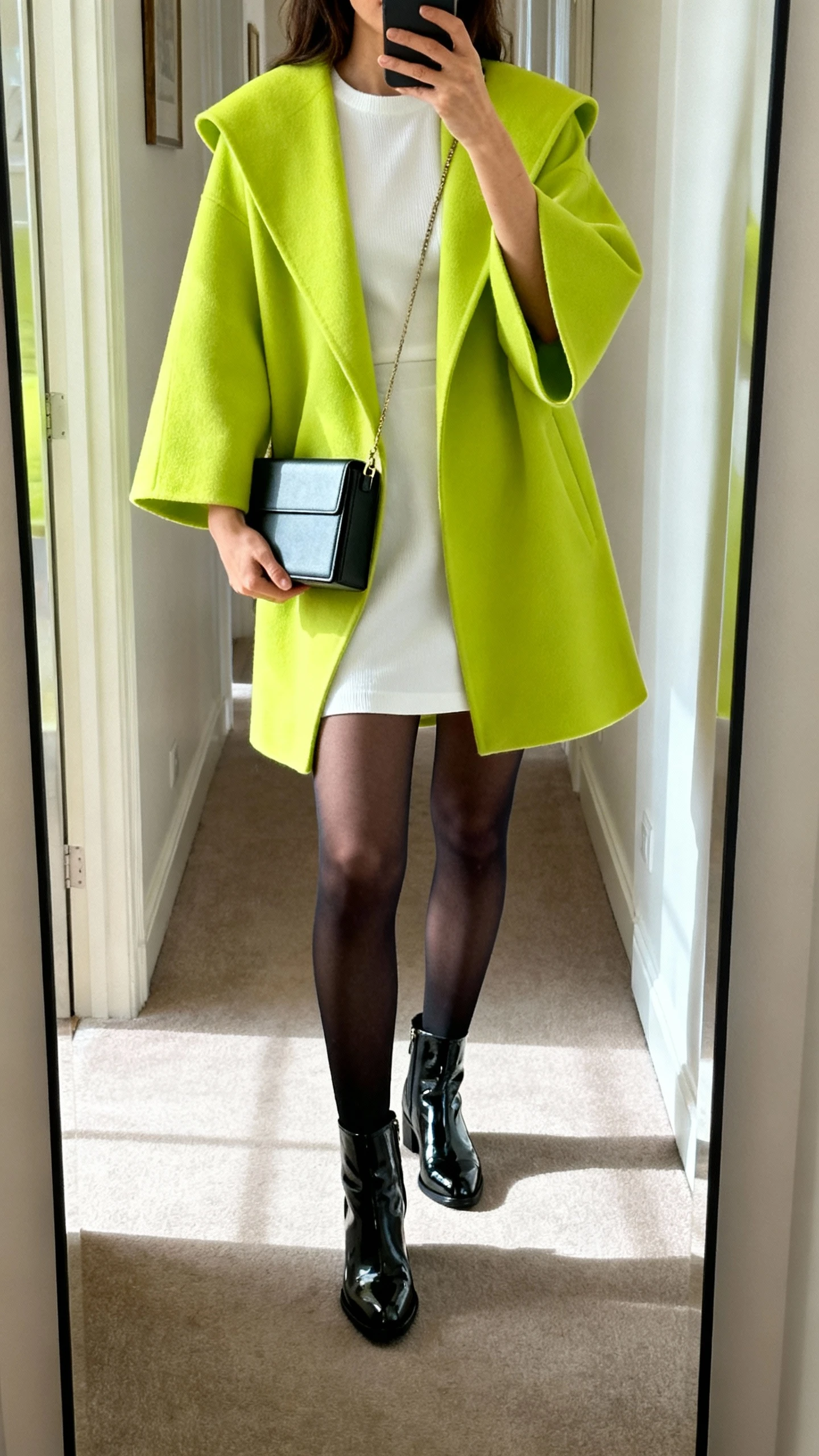 iPhone mirror selfie of a woman wearing a white go-go mini dress, a swing coat in bright color, opaque black tights, patent ankle boots, and a small boxy handbag, face not visible, cropped at neck, hallway full-length mirror with natural daylight, iPhone photo quality.