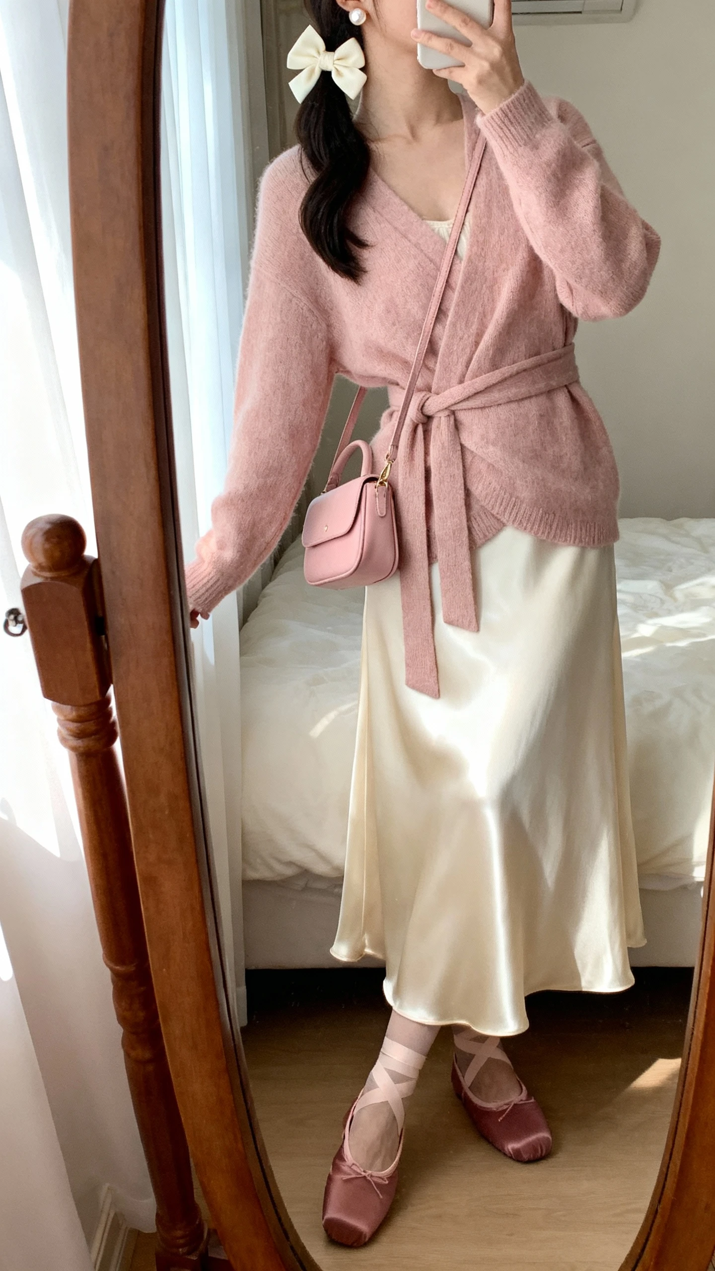 iPhone side-angle mirror selfie of a woman wearing soft balletcore: blush wrap cardigan, cream satin midi skirt, dusty rose ballet flats, cream hair bow, delicate pearl studs, blush mini shoulder bag; face not visible, cropped at shoulders, bedroom mirror, gentle window light, iPhone photo quality.