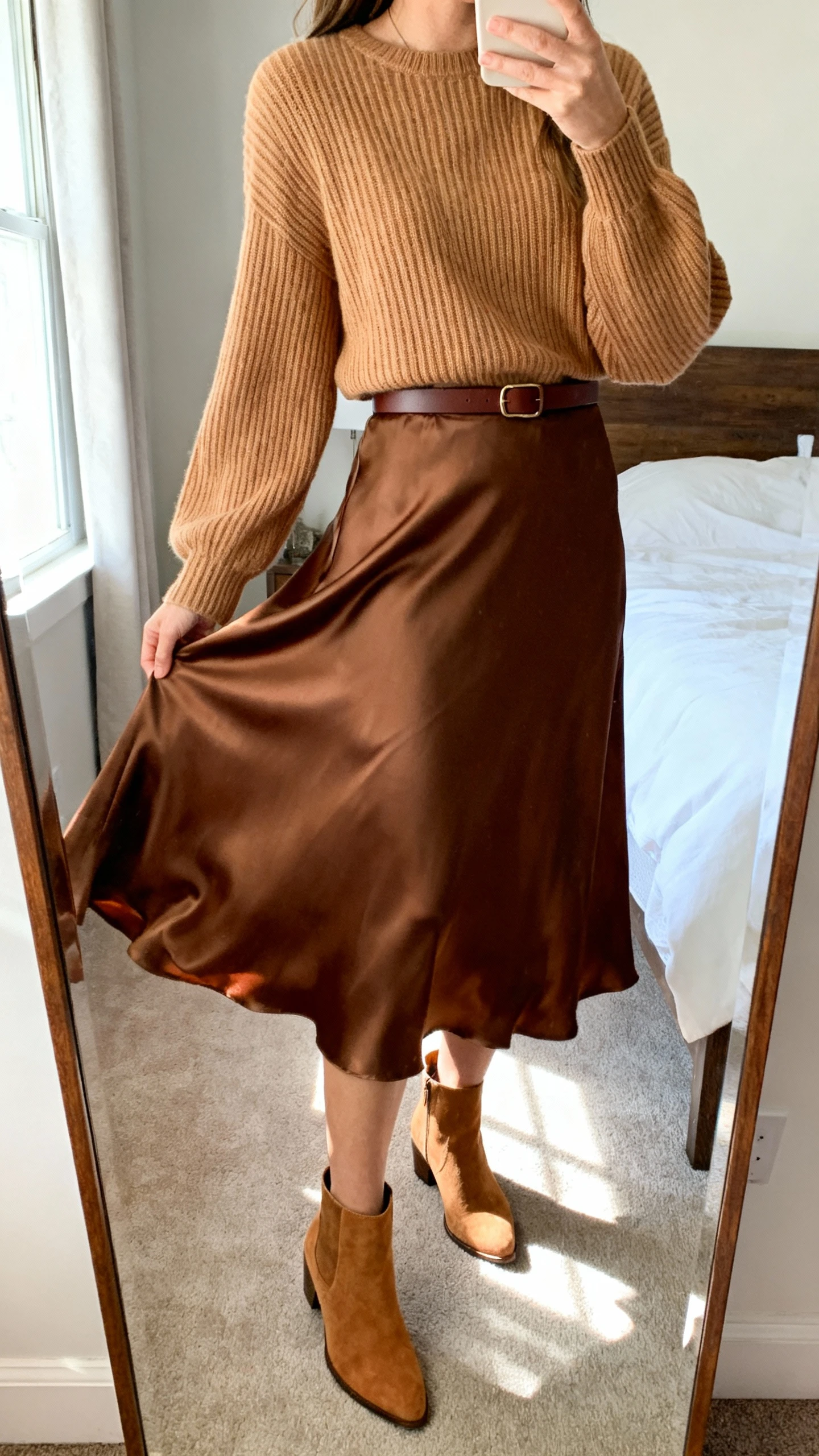 iPhone side-angle mirror selfie of a woman wearing a hazelnut ribbed knit sweater tucked into a mocha satin midi skirt that twirls, with tan ankle boots and a slim chocolate belt, face not visible, cropped at shoulders, bedroom mirror, natural afternoon light, iPhone photo quality.