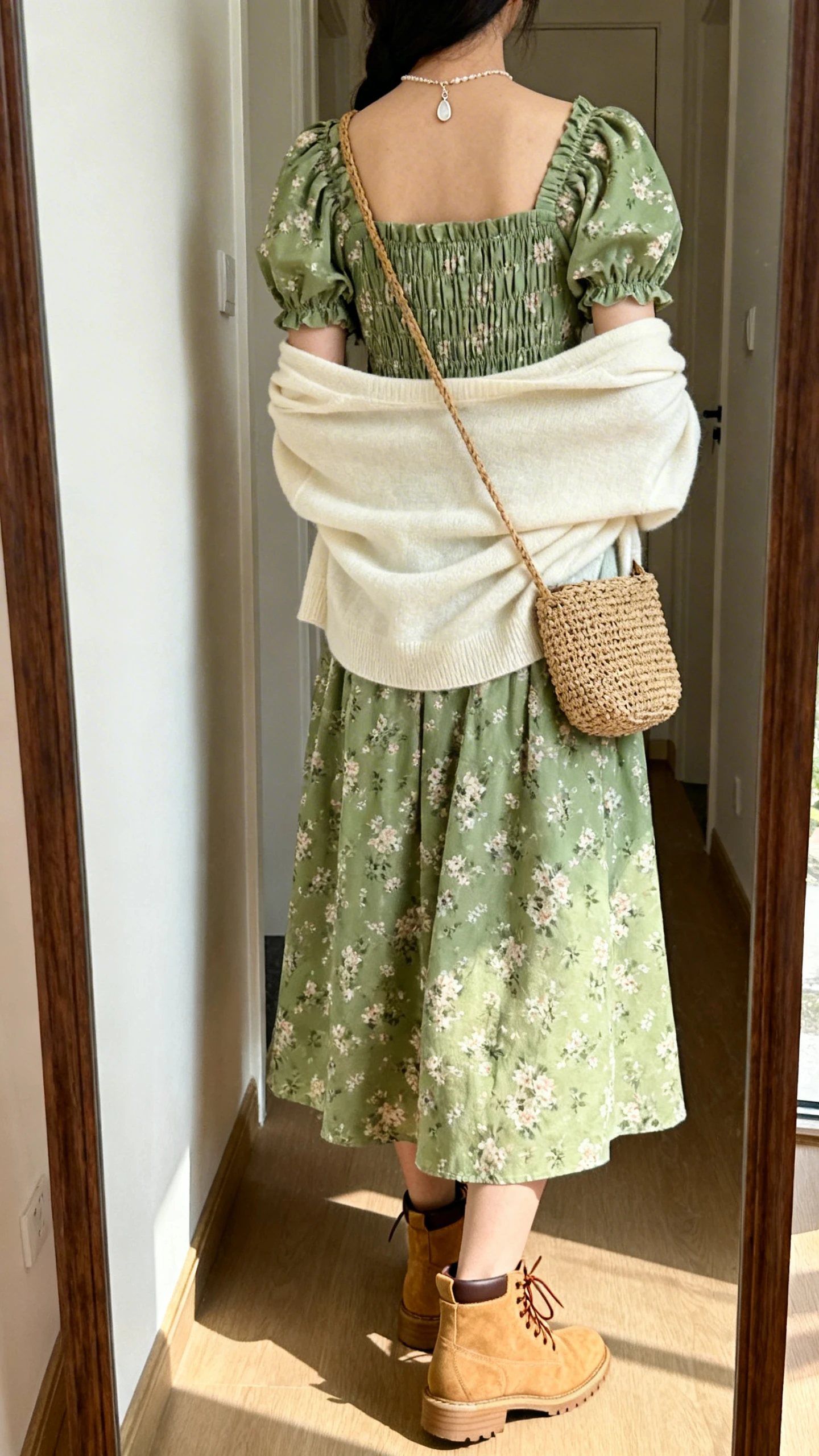 iPhone back view of a woman wearing a modern cottagecore outfit: sage green floral midi dress with puff sleeves and a smocked bodice, cream cardigan draped over shoulders, tan lace-up ankle boots, dainty pendant necklace, and a woven crossbody, face not visible, hallway full-length mirror, morning light, iPhone photo quality.