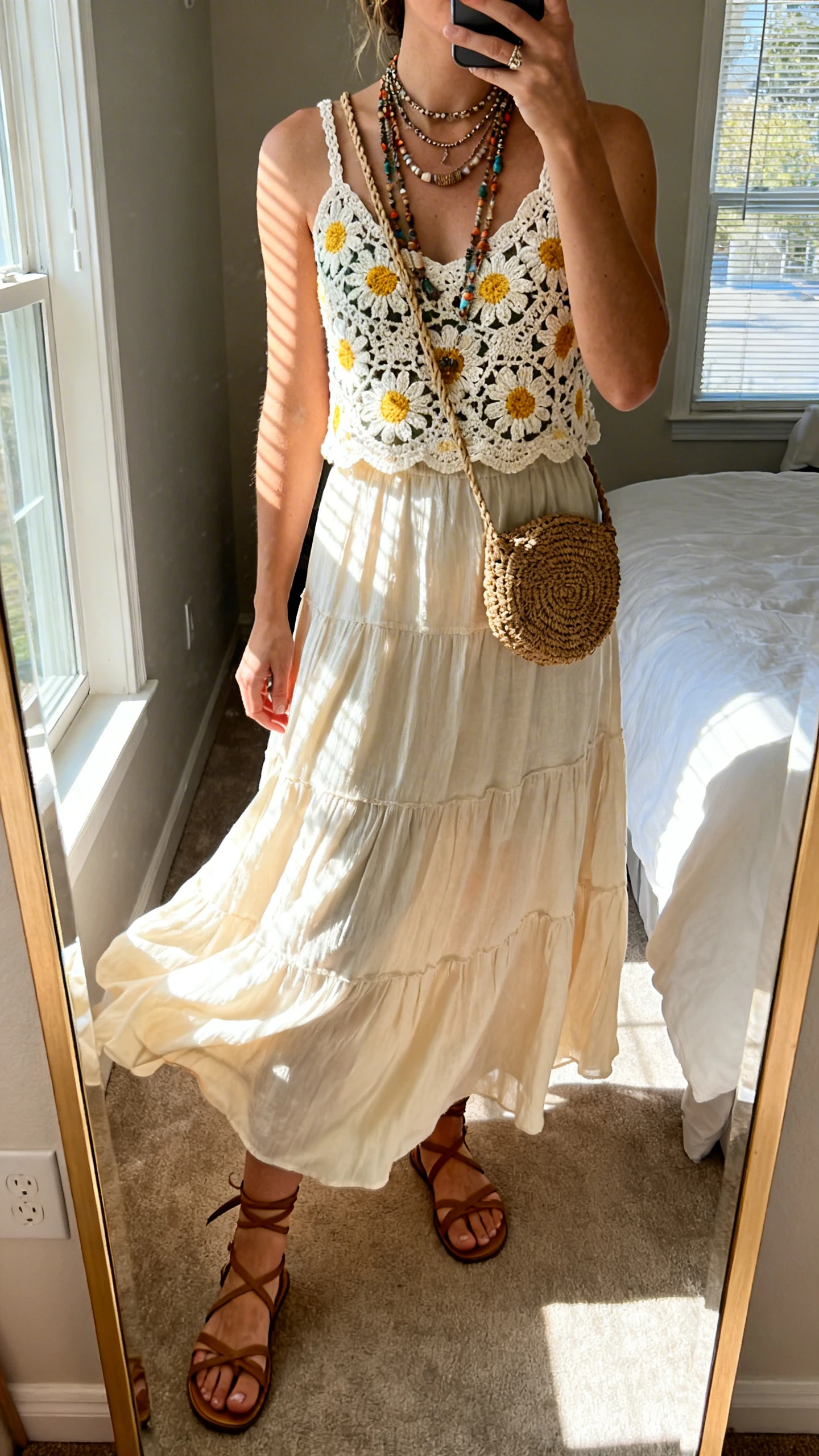 iPhone mirror selfie of a woman wearing a sunlit daisy crochet top with a flowy maxi skirt that swishes, strappy sandals, layered boho necklaces, and a woven crossbody, face not visible, cropped at neck, bedroom mirror, natural window light, iPhone photo quality.