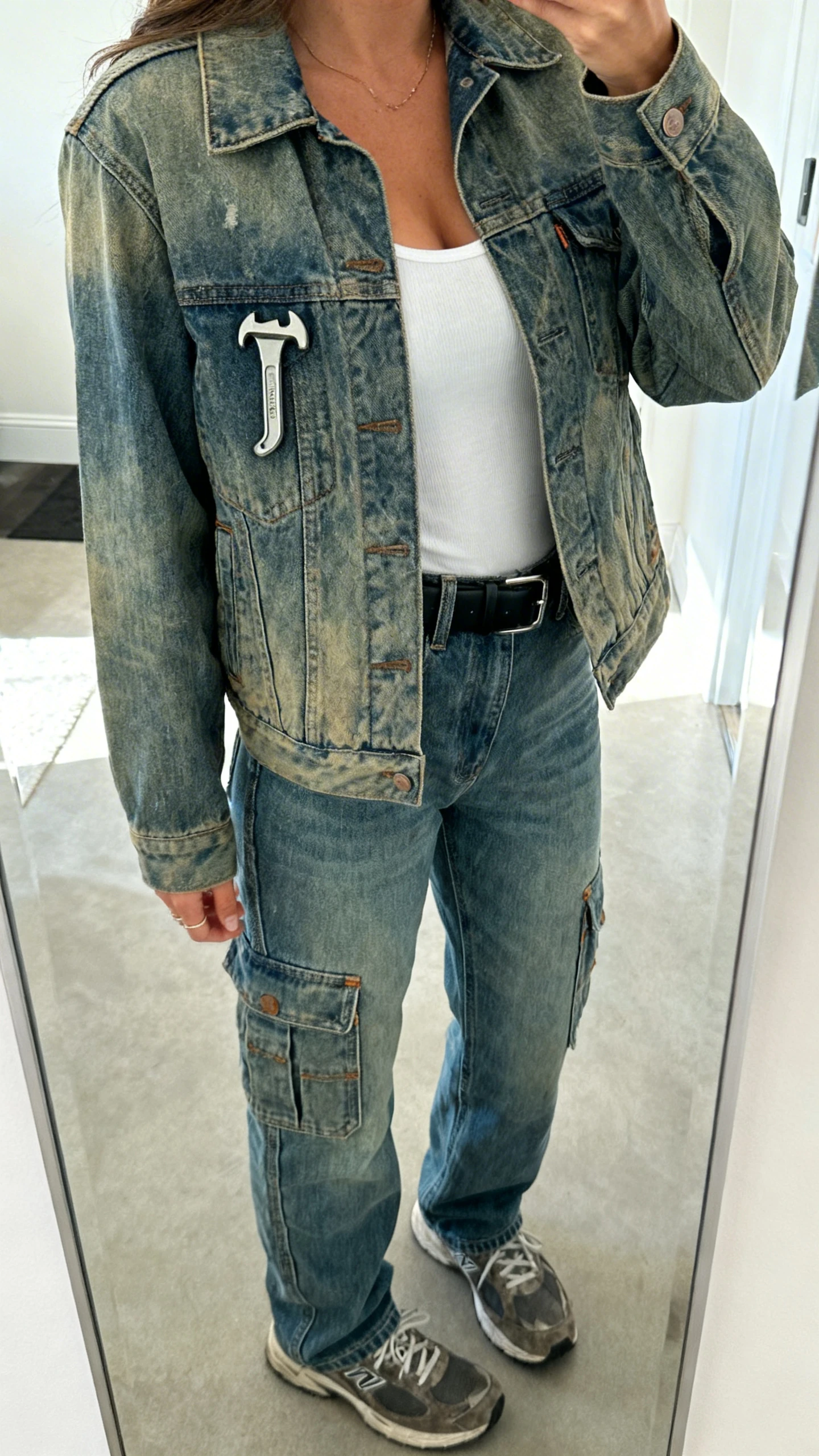 iPhone mirror selfie of a woman wearing double denim: a faded trucker jacket with carpenter jeans (hammer loop and pockets visible), white tank underneath, black belt, and rugged sneakers, face not visible, cropped at shoulders, full-length mirror, natural daylight, iPhone photo quality.